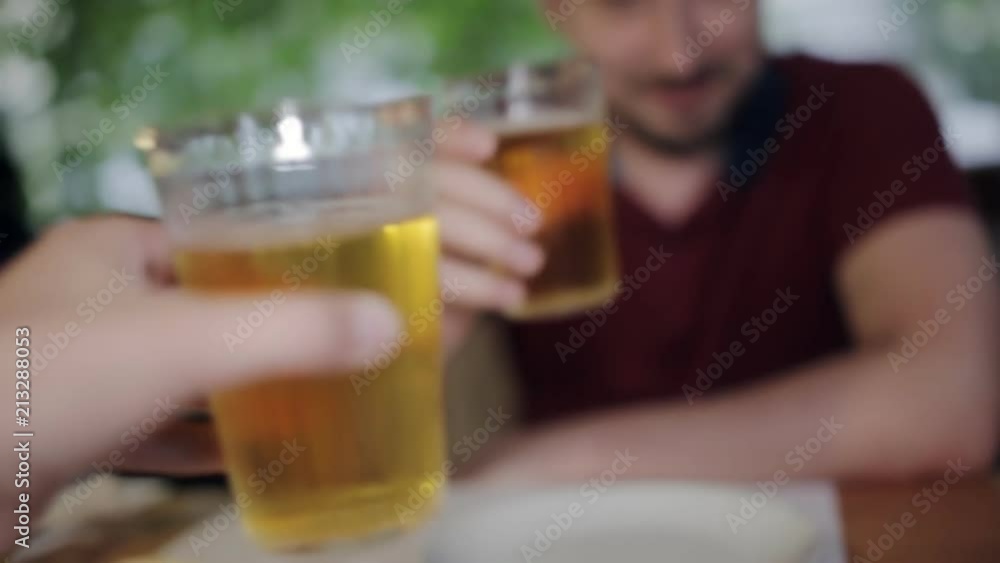 A young man sitting with a friend in a pizzeria drinking beer clinking glasses. Communication after a working day A young man sitting with a friend in a pizzeria drinking beer clinking glasses. Communication after a working day