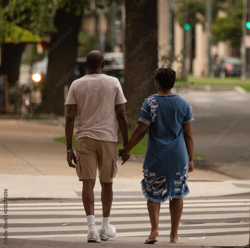 unknown happy couple holds hands as they walk downtown