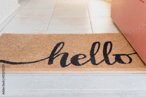 Open door with a natural fiber rug with the word hello written in script