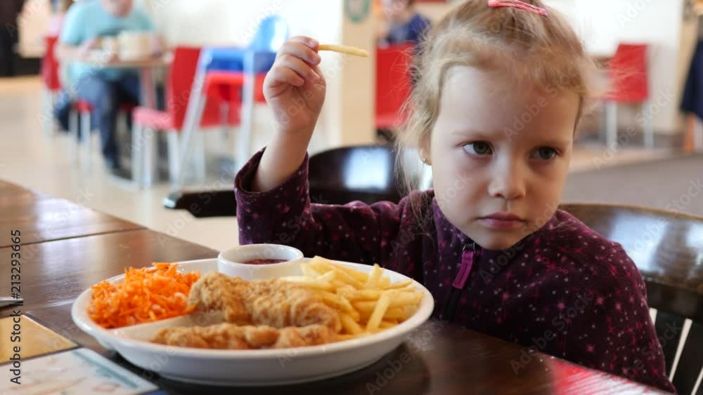Cute little kid girl portrait funny eating french fries in fast food court of a mall Cute little kid girl portrait funny eating french fries in fast food court of a mall