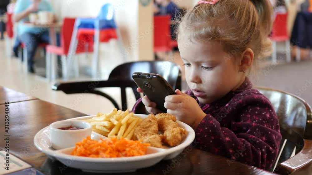 Little kid girl make dish photo via smart phone during eating in fast food court Little kid girl make dish photo via smart phone during eating in fast food court