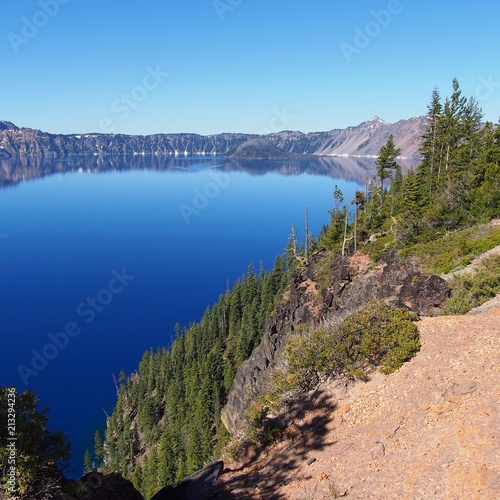 The magnificent rich blue waters of Crater Lake with reflections of the rim in the forests of Southern Oregon on a beautiful sunny summer morning. 