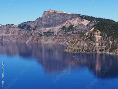 The magnificent rich blue waters of Crater Lake with reflections of the rim in the forests of Southern Oregon on a beautiful sunny summer morning. 