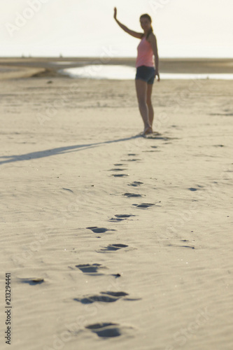 A young girl is seen from behind as she walks, leaving footprints in the sand