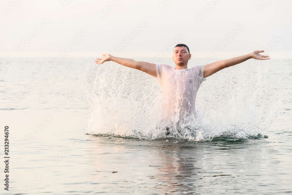 A young man jumps out of the water with his hands raised to the sides