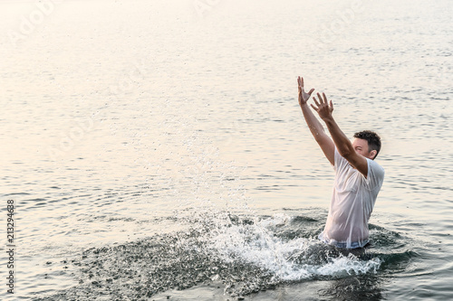 A young man standing on the waist in the sea created a very high wall of splashes with the movement of his hands