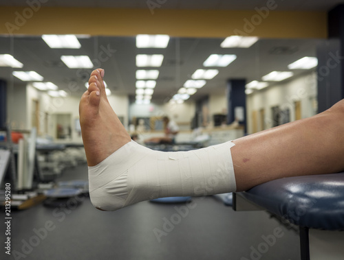 Athlete's foot with an ankle tape job for support hanging off a table in a medical clinic 