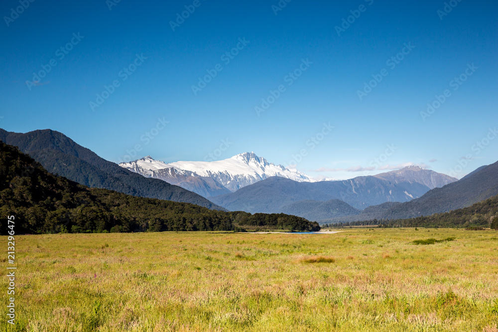 Mount Cook stands above a ssmall er mountain range, river and meadow on the south island of New Zealand