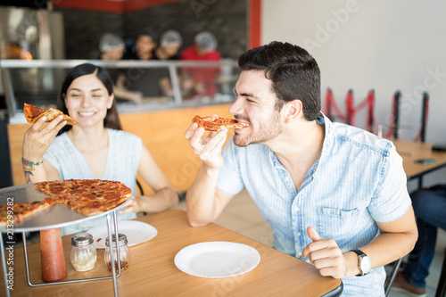 Handsome latin man enjoying eating pizza slice in pizza shop