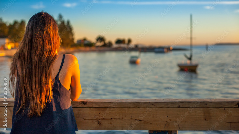 Young lady watching boats sailing away at dusk.