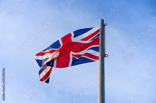Waving or Flying United Kingdom's Flag caled Union Jack on steel pool with blue sky at back