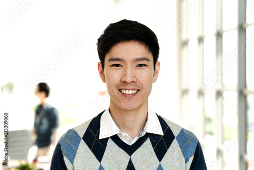 Portrait of young attractive asian creative man smiling and looking at camera in modern office feeling confident and positive. Headshot of chinese male employee, entrepreneur or college student.