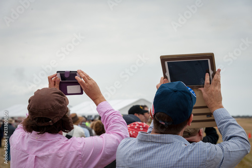 Two airshow spectators taking photographs with their hand held devices