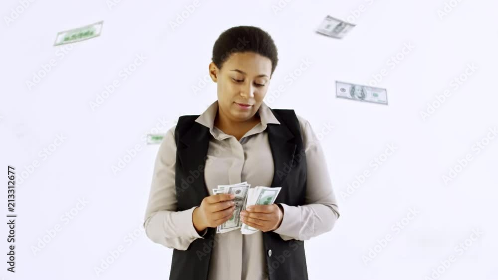 Cinemagraph of pensive black woman standing against isolated white background and looking at cash money; banknotes falling from ceiling Cinemagraph of pensive black woman standing against isolated white background and looking at cash money; banknotes falling from ceiling