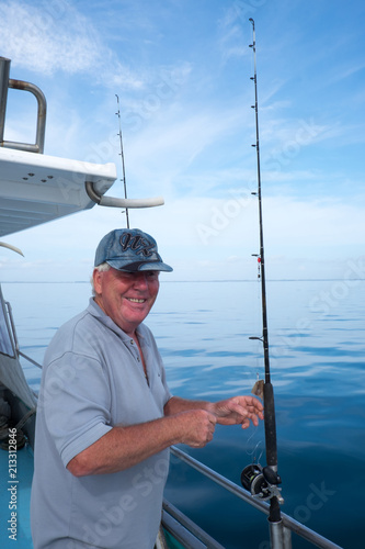 Happy mature smiling tourist on fishing boat charter with rod in Doubtless Bay, Far North, New Zealand, NZ