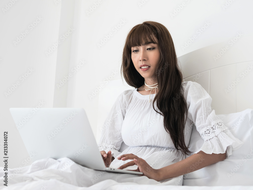 Happy casual beautiful asian woman lying on bed using laptop in bedroom at home Happy casual beautiful asian woman lying on bed using laptop in bedroom at home