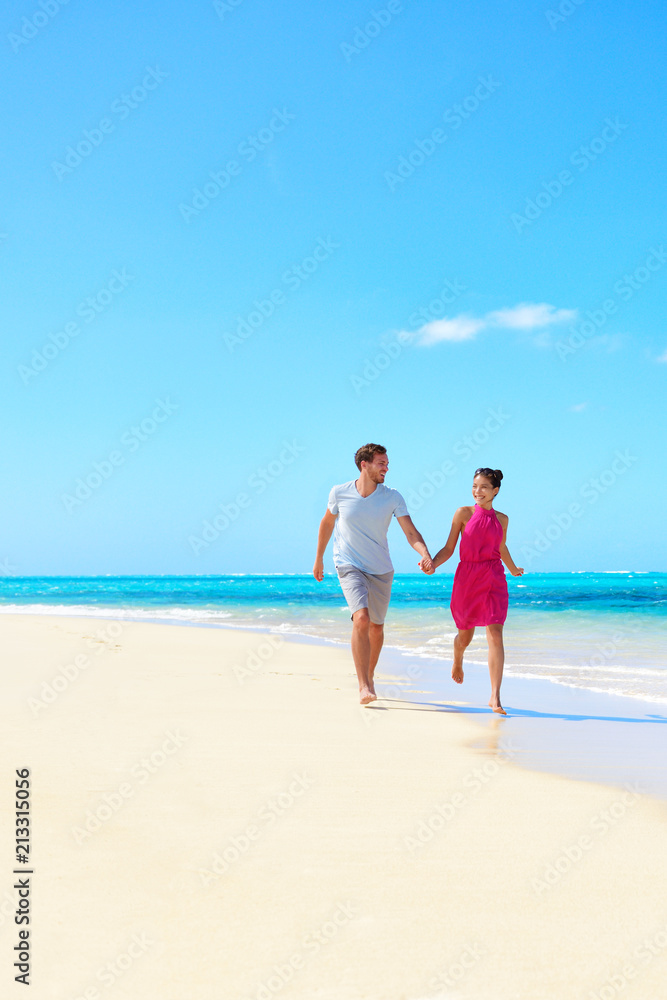 Luxury beach travel vacation couple walking in love during honeymoon getaway on paradise tropical destination. Woman and man running of joy holding hands.