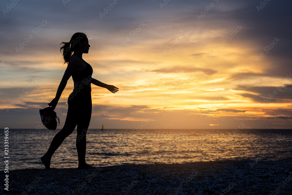 Woman hold the shoes walking on beach for exercise at sunset time. healthy concept.