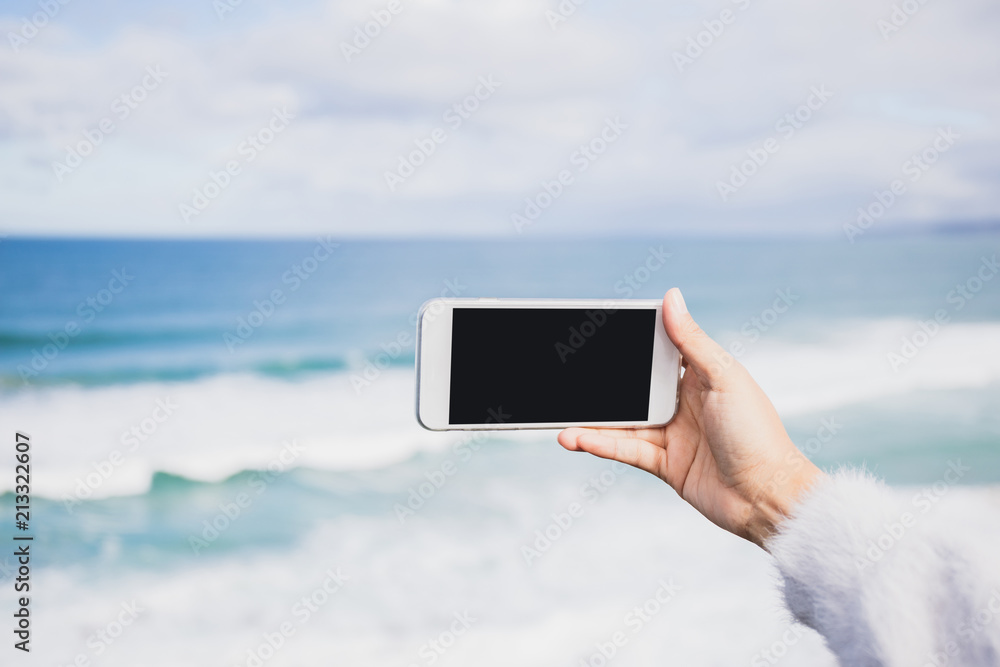 Woman hands holding and using smartphone with blank screen for your text or advertising on blurred blue sea background.Mock up phone mobile concept.