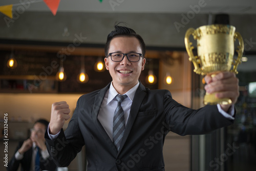 Asian businessman raising up hand and holding a golden trophy cup to cheerful and celebrated his successful in mission. concept of winner and competition. photo