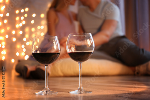 Glasses of red wine and blurred loving couple on background