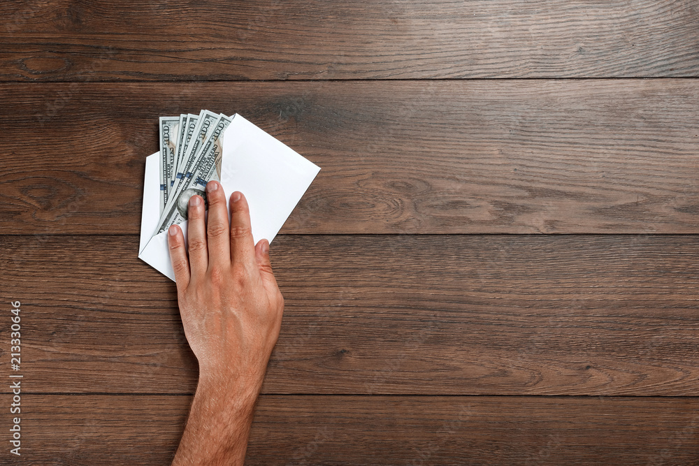 Man's hand and dolors of the USA in a white envelope, Top view, on a wooden table. The concept of income, bonuses or bribes. Corruption, salary, bonus.