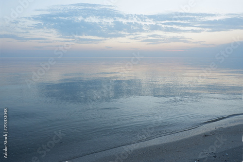 Calm down the sea at dawn. Bright blue water with a pink luster. The sky is in the water.