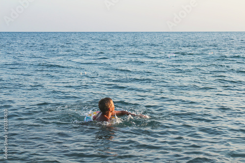 Teen boy bathes in the sea, big waves and sea foam.