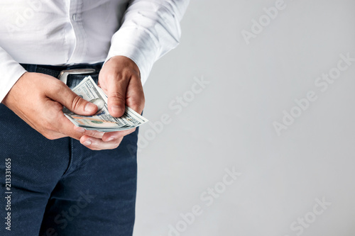Male hands of businessman counting dollars close-up, light background.