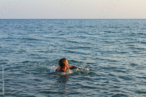 Teen boy bathes in the sea, big waves and sea foam.