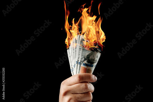 Male hand close-up, holds burning money in hands, burning US dollars. Black background, isolate. The concept of inflation, a decrease in the purchase of foreign currency, and devolution. photo