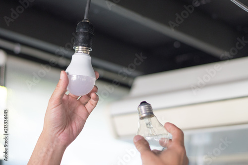 Power saving concept. Asia man changing compact-fluorescent (CFL) bulbs with new LED light bulb. photo