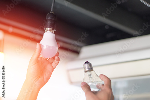 Power saving concept. Asia man changing compact-fluorescent (CFL) bulbs with new LED light bulb.