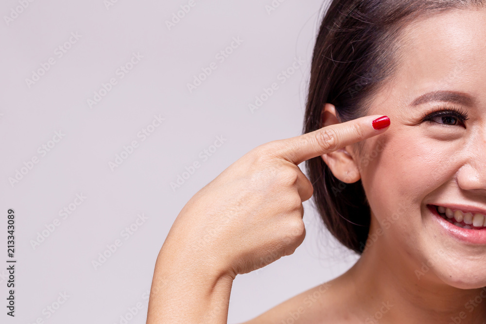 Adult beautiful Asian woman smiling while fingering and pointing at the wrinkles on around aging eyes in white background - with copy space. Adult beautiful Asian woman smiling while fingering and pointing at the wrinkles on around aging eyes in white background - with copy space.