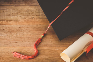 martarboard or graduation cap with red tassel and diploma tied with red ribbon on wooden table, vintage tone
