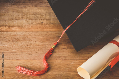 martarboard or graduation cap with red tassel and diploma tied with red ribbon on wooden table, vintage tone