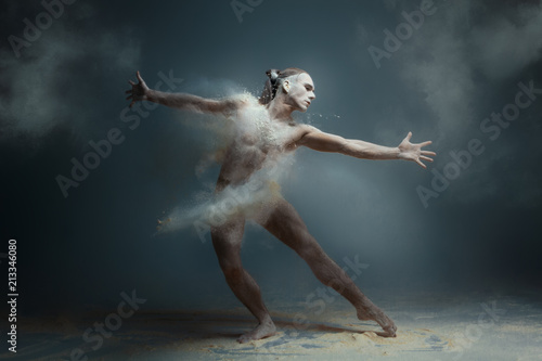 Dancing in flour concept. Long hair muscle fitness guy man male dancer in dust / fog. Guy wearing white shorts making dance element in flour cloud on isolated grey background