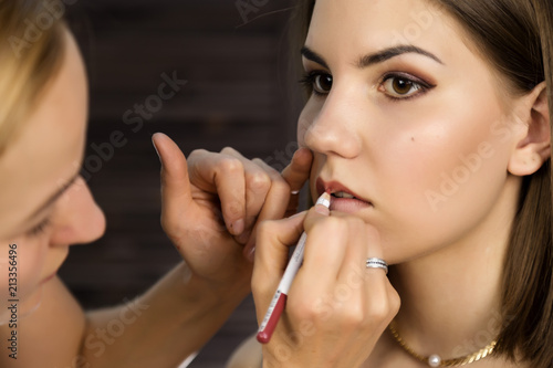 make-up artist apply pink glitter on lipstick with brush on a woman s lips