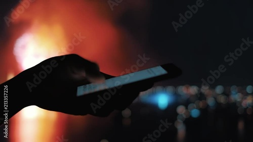 Closeup on the silhouette of a woman's hand sending a message on a mobile phone with fireworks in background, shoot in HD 1920p photo