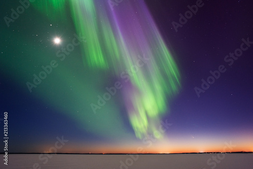 Northern Lights and Moon above frozen lake after sunset in eastern Finland