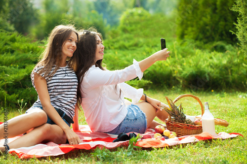 Two young girls having fun on the picnic, making selfie on a smartphone photo