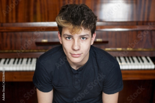 A cute teen smiles against a piano background. He had a good mood because he played well at the concert photo