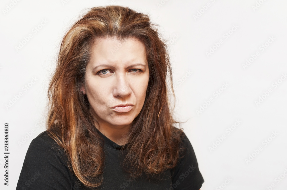 Cute middle-aged woman on gray background angry as her hair starts to become gray Cute middle-aged woman on gray background angry as her hair starts to become gray