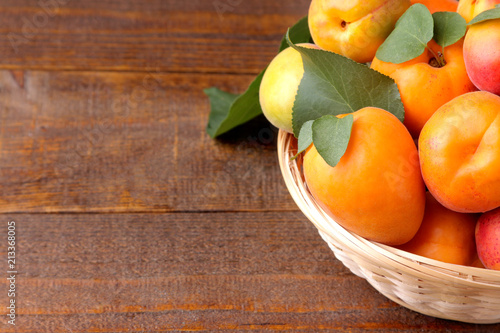 A lot of fresh, ripe apricot in a wicker basket on a brown wooden background