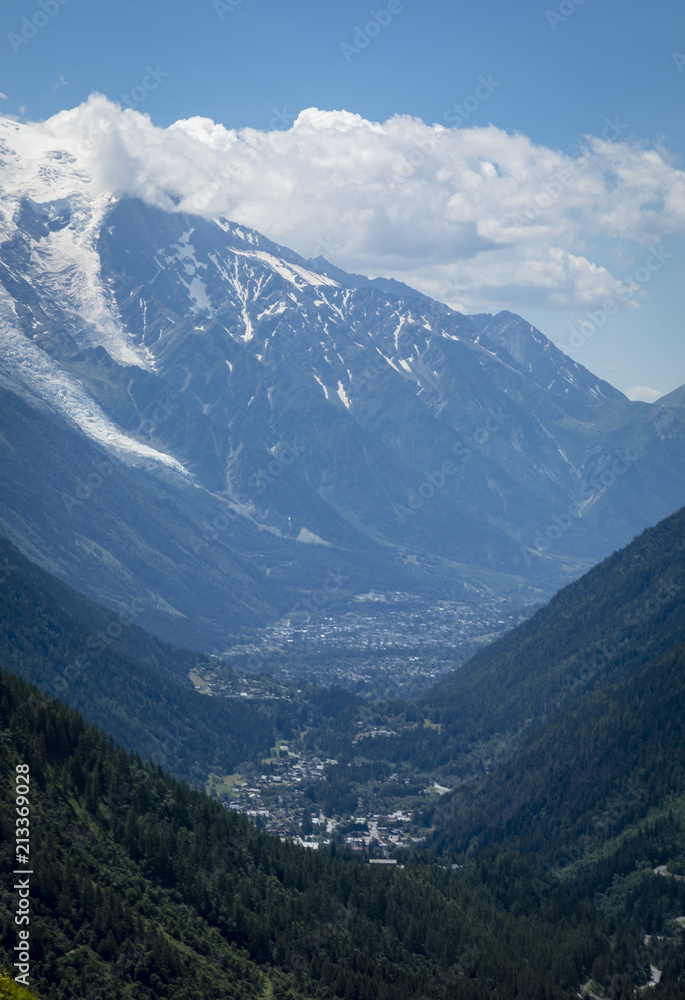 a view of the chamonix valley from the alpine mountains in the Vallorcine area with foreground of alpine meadows on a clear summer day with blue sky and bright clouds