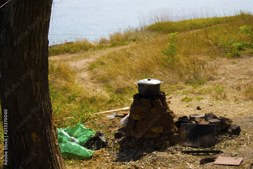 Bowler on a homemade stone hearth under a tree in the middle of grass and the sea. The concept of an ideal holiday in nature. Bowler on a homemade stone hearth under a tree in the middle of grass and the sea. The concept of an ideal holiday in nature.