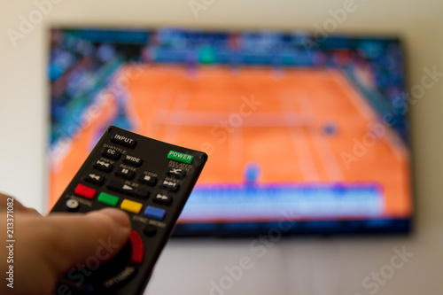 Close-up macro of man's hand with TV remote control watching a tennis match