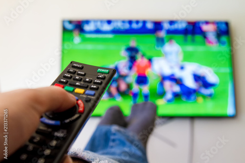 Close-up macro of man's hand with TV remote control watching a rugby match photo