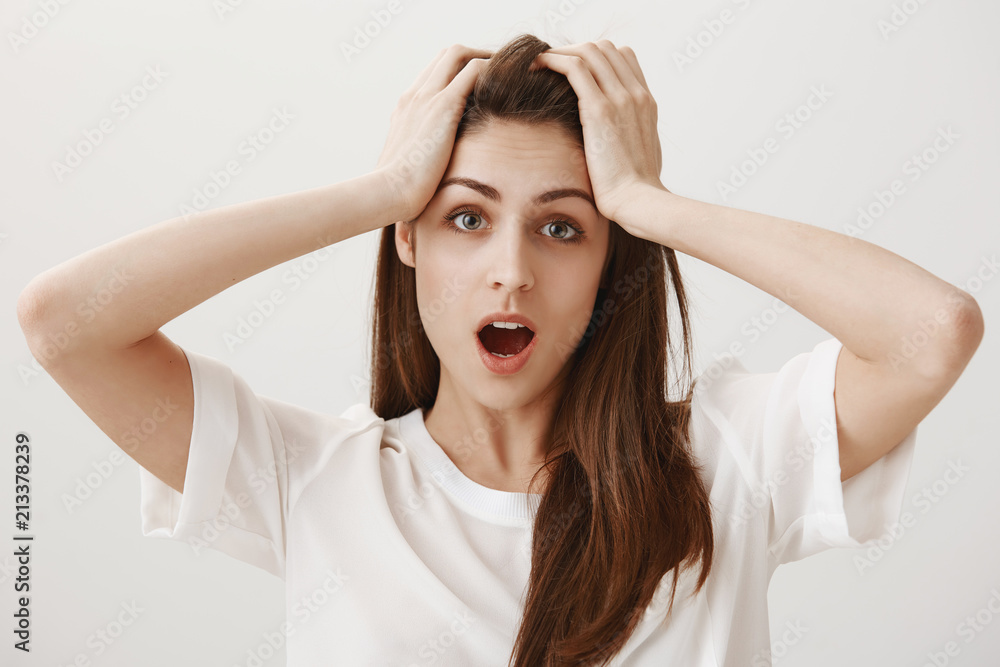 Deadline is near. Portrait of trobled and stressed attractive young woman holding hands on head and dropping jaw, being shocked with loads of work that need to tackle alone, standing over gray wall Deadline is near. Portrait of trobled and stressed attractive young woman holding hands on head and dropping jaw, being shocked with loads of work that need to tackle alone, standing over gray wall