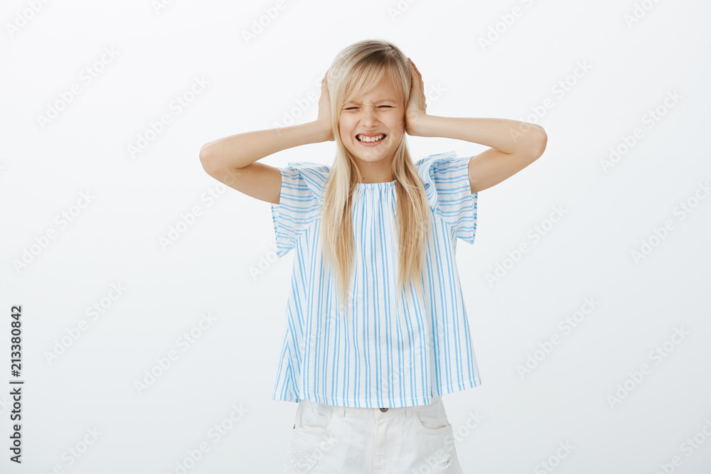 Daughter hates hearing parents fight. Portrait of upset fed up young girl with fair hair, grimacing from dislike, covering ears with palms, distracted and annoyed with loud noise from street Daughter hates hearing parents fight. Portrait of upset fed up young girl with fair hair, grimacing from dislike, covering ears with palms, distracted and annoyed with loud noise from street